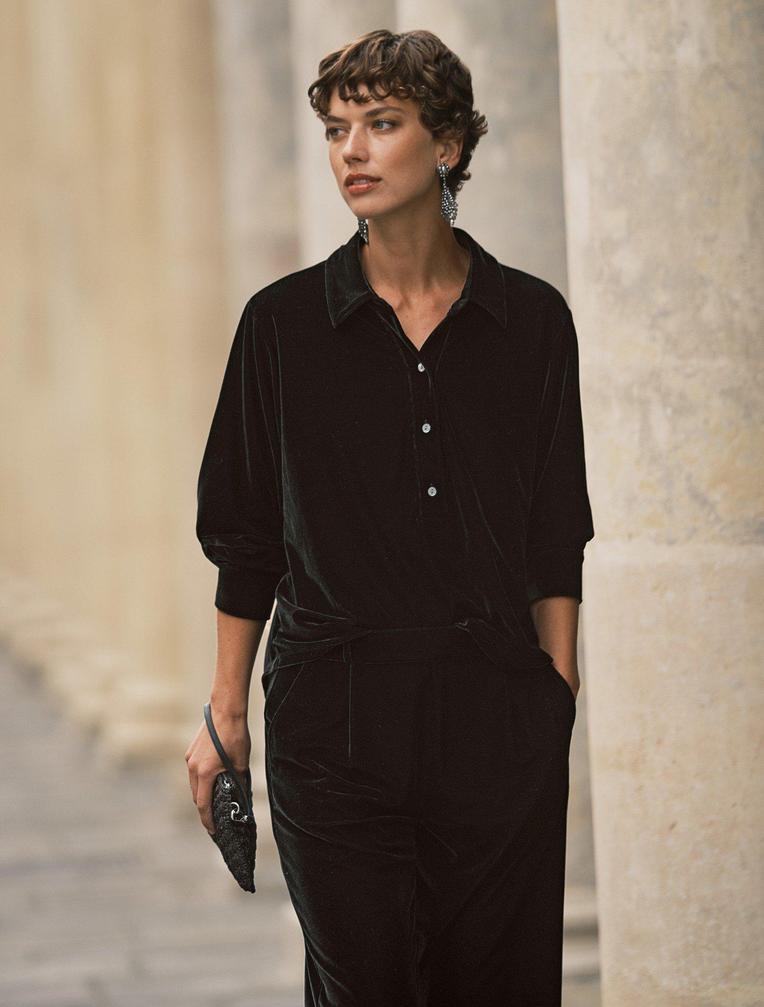 a woman in black dress walking down a street with a purse